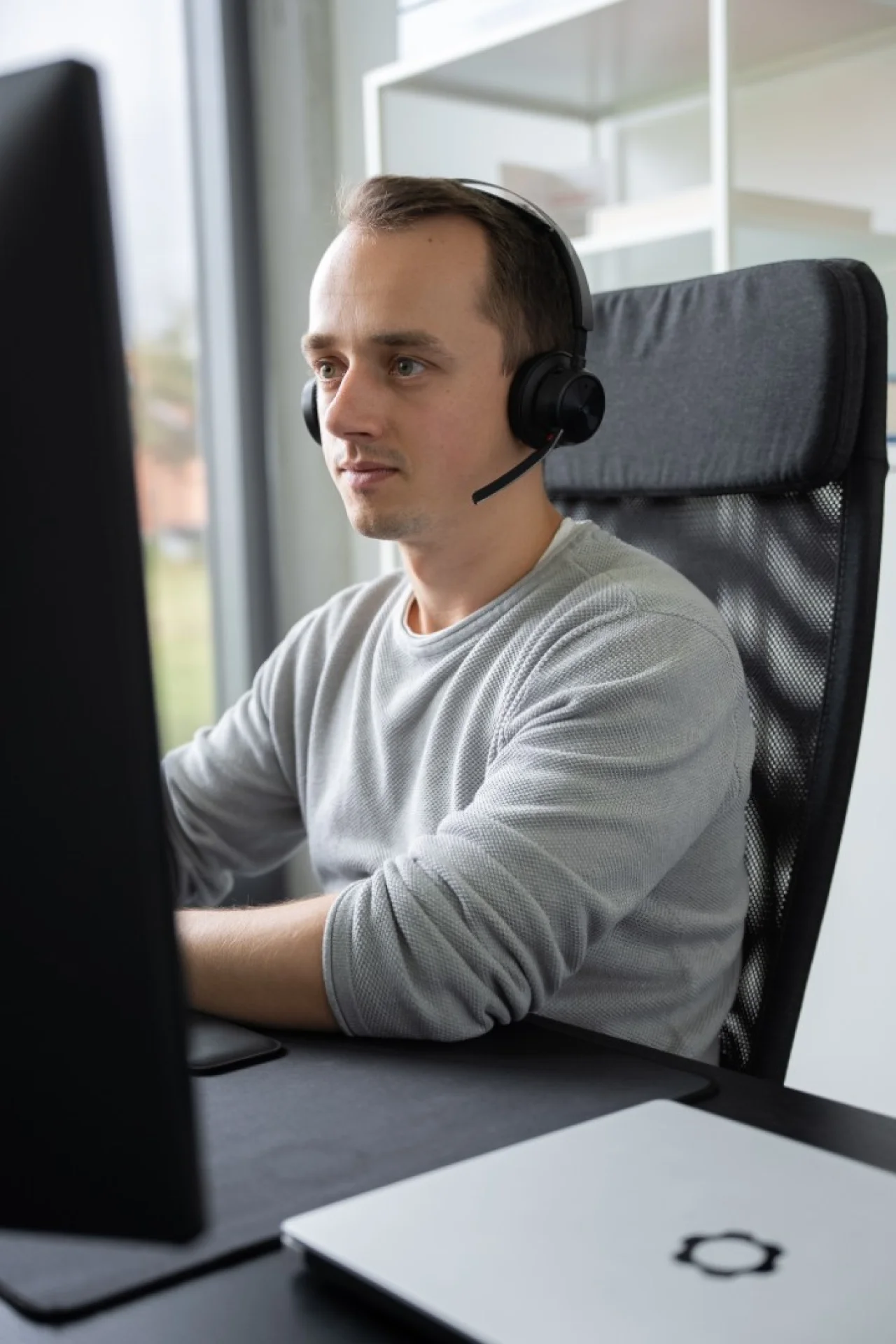 Mann mit Headset sitzt an Schreibtisch vor Computer und schaut konzentriert auf den Bildschirm.