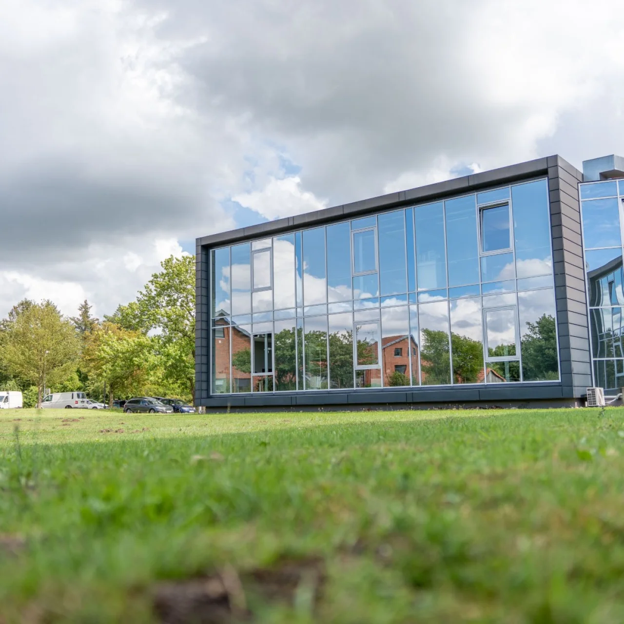 Die verspiegelte Glasfront eines modernen Bürogebäudes an einem sonnigen Tag mit Rasenfläche davor.