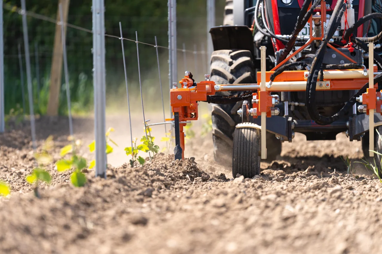 Landwirtschaftliche Maschine mit Reifen und Metallgestell bearbeitet einen Acker mit jungen Pflanzenreihen.